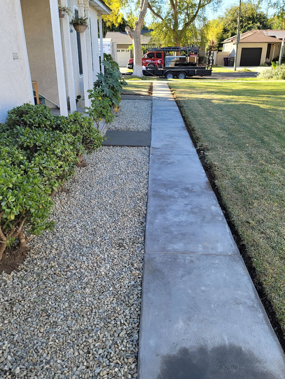 Concrete sidewalk alongside landscaped yard and gravel path near residential home.