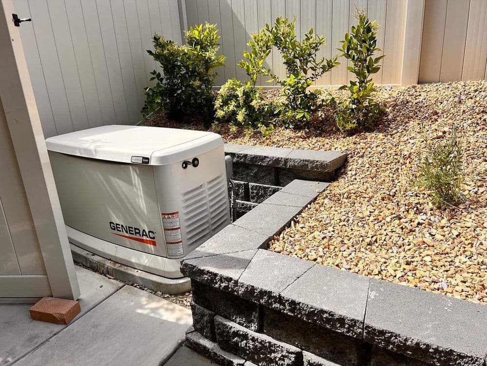 Generac generator installed in landscaped yard with gravel and low bushes.