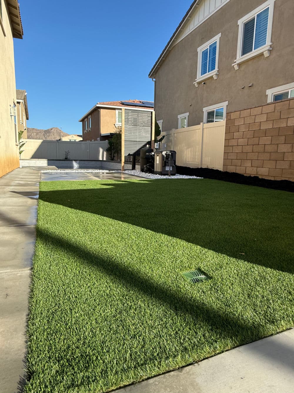 Lush green artificial turf backyard with mountains in the background and modern homes.