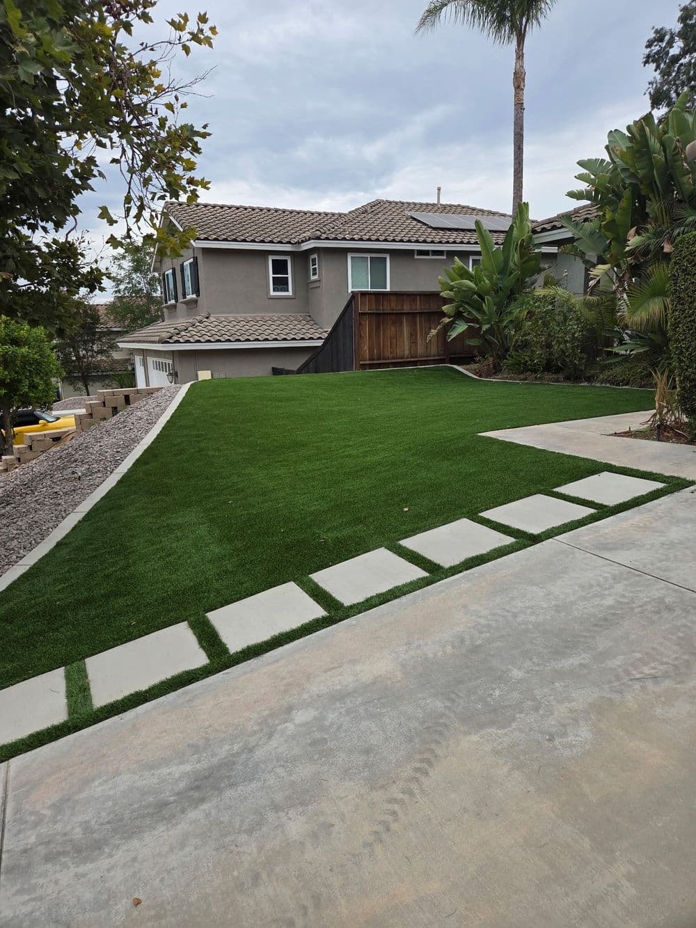 Lush green artificial turf in a landscaped backyard with stone pathway and modern home.